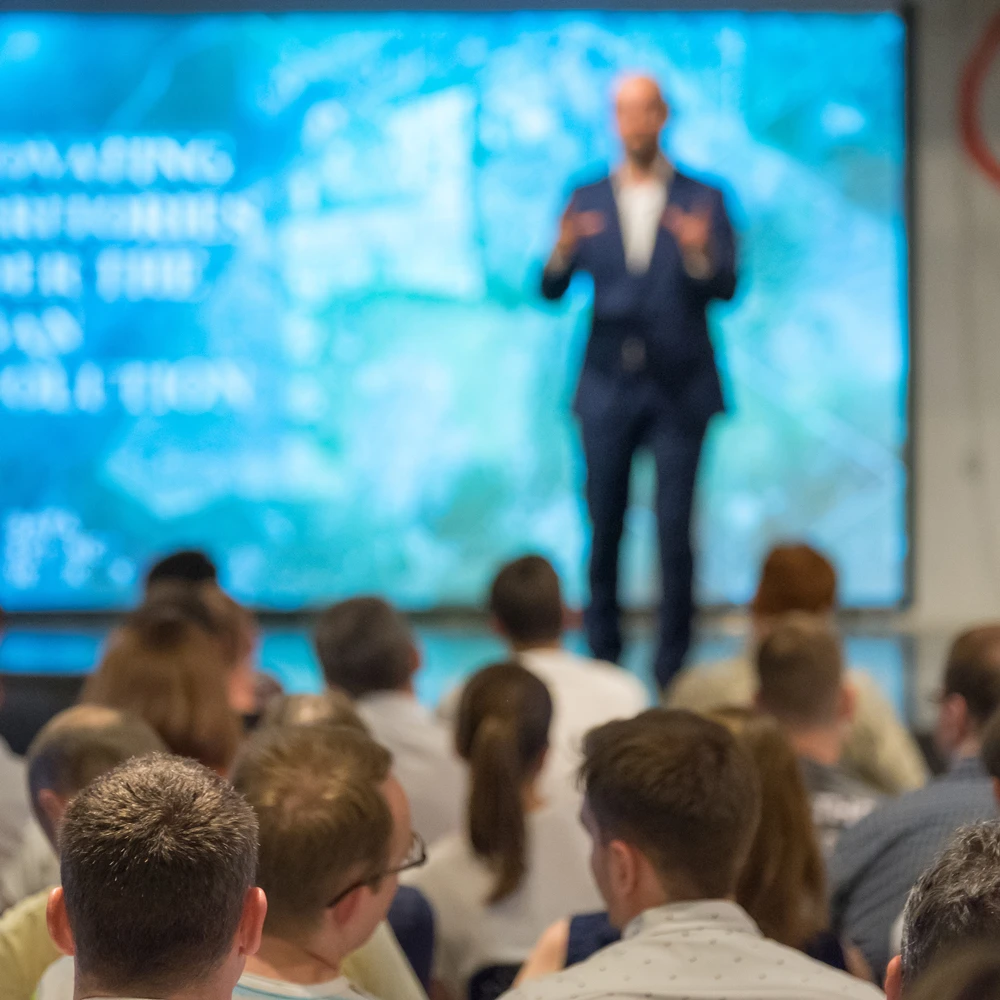 A man speaking in front of a crowd at a XYMOGEN-hosted conference